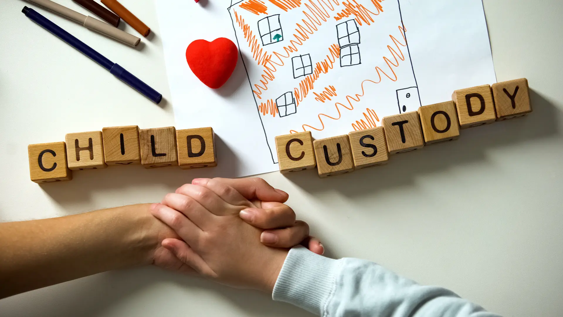 Child and parent holding hands with letter blocks spelling “CHILD CUSTODY” in a children’s playroom setting.